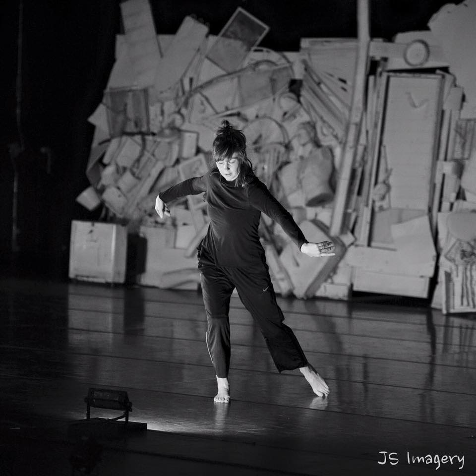 A dancer extends her right foot with her arms out to the sides as she rehearses on a stage